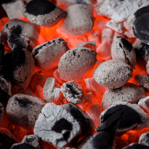 Close-up of glowing embers of charcoal briquettes, showing white ash-covered coals with bright orange-red heat radiating beneath